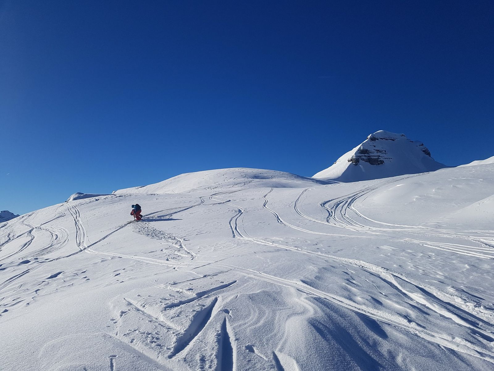 A lone skier on a sunny slope below a snowy peak at Grand Massif, France